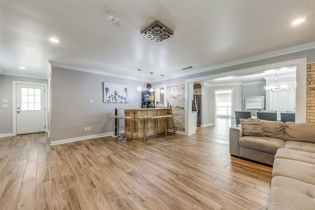 living room featuring ornamental molding, light wood-type flooring, an inviting chandelier, and bar area