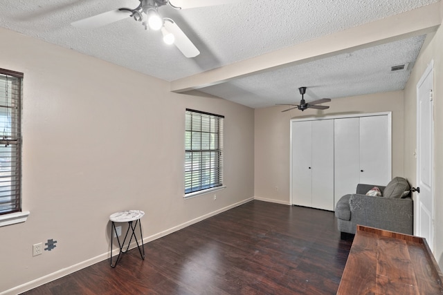 living area featuring ceiling fan, beamed ceiling, a textured ceiling, and dark wood-type flooring