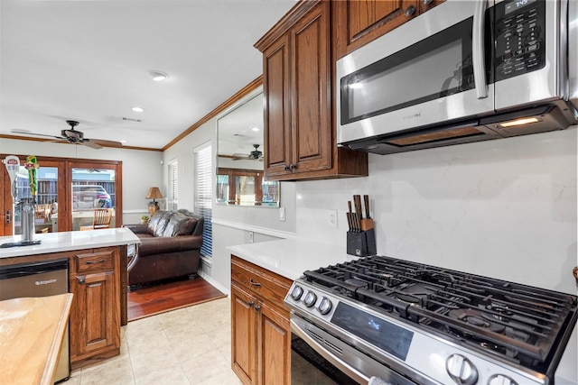 kitchen with appliances with stainless steel finishes, light tile patterned floors, ceiling fan, and ornamental molding