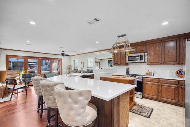 kitchen with decorative light fixtures, stainless steel appliances, a breakfast bar area, and an island with sink