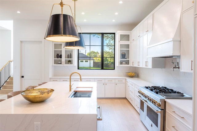 kitchen with pendant lighting, sink, white cabinets, range with two ovens, and custom range hood