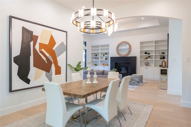 dining room with built in shelves, a raised ceiling, and light wood-type flooring