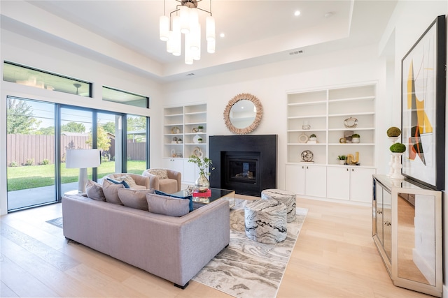 living room featuring built in shelves, a tray ceiling, an inviting chandelier, and light hardwood / wood-style flooring