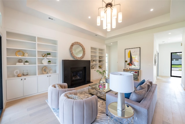 living room with an inviting chandelier, a tray ceiling, built in features, and light wood-type flooring