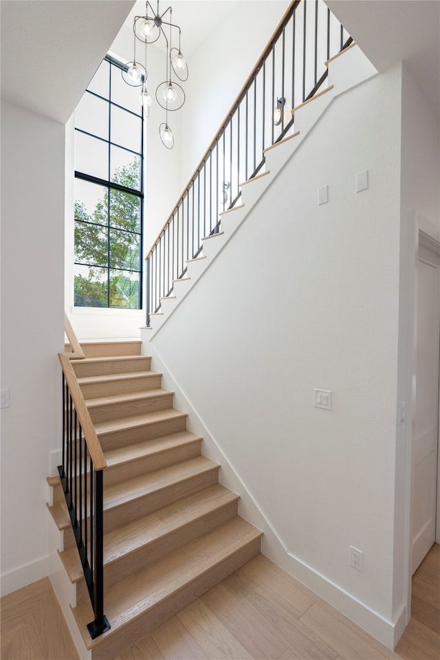 stairs featuring a chandelier, hardwood / wood-style floors, and a high ceiling