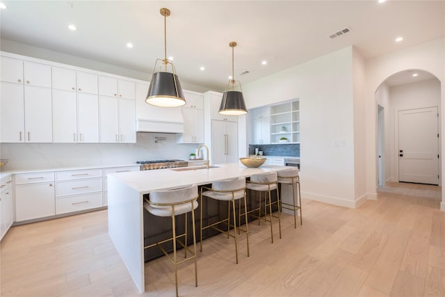 kitchen featuring a breakfast bar, sink, hanging light fixtures, a kitchen island with sink, and white cabinets