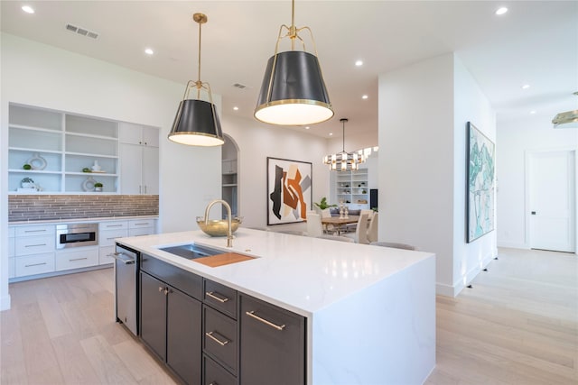 kitchen with sink, decorative light fixtures, light wood-type flooring, a kitchen island with sink, and white cabinets