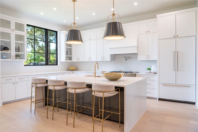 kitchen featuring white cabinetry, paneled fridge, and an island with sink