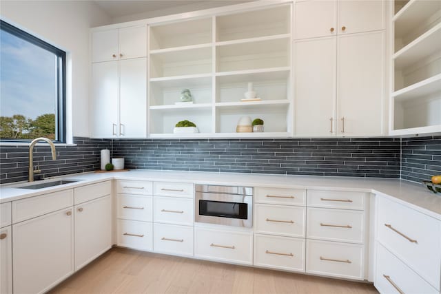 kitchen featuring tasteful backsplash, white cabinetry, sink, and light hardwood / wood-style floors