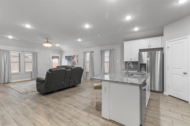 kitchen featuring appliances with stainless steel finishes, light stone counters, a kitchen island with sink, sink, and white cabinets