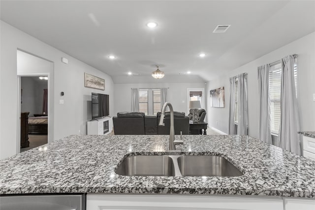 kitchen with white cabinetry, sink, dark stone counters, and a center island with sink