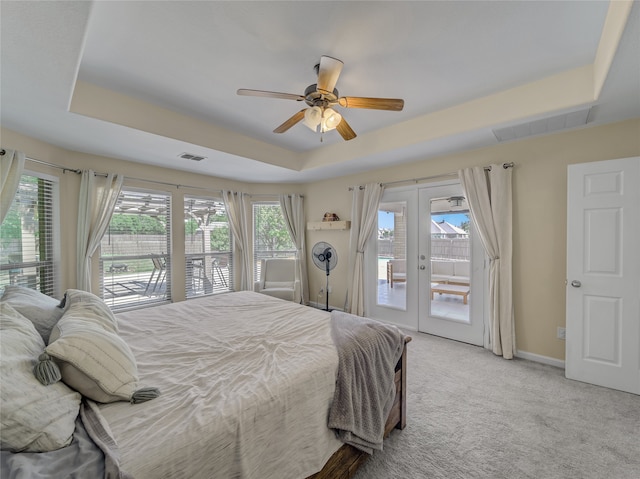 carpeted bedroom with access to exterior, multiple windows, ceiling fan, and a tray ceiling