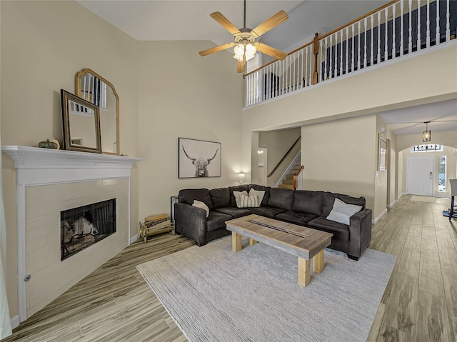 living room with ceiling fan, high vaulted ceiling, a tiled fireplace, and light hardwood / wood-style flooring