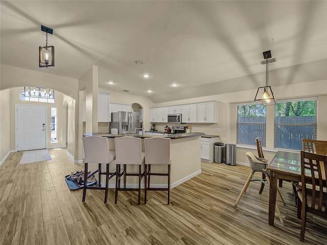 kitchen featuring light hardwood / wood-style floors, a kitchen breakfast bar, decorative light fixtures, stainless steel appliances, and white cabinetry