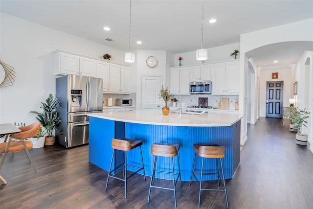 kitchen with appliances with stainless steel finishes, a center island with sink, dark hardwood / wood-style floors, white cabinetry, and hanging light fixtures