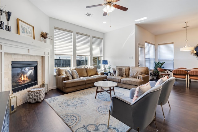 living room with ceiling fan, dark hardwood / wood-style flooring, a wealth of natural light, and a tiled fireplace