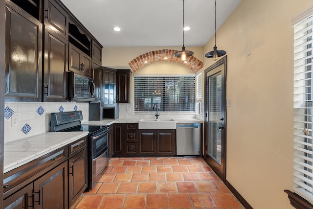 kitchen featuring appliances with stainless steel finishes, sink, backsplash, hanging light fixtures, and dark brown cabinetry