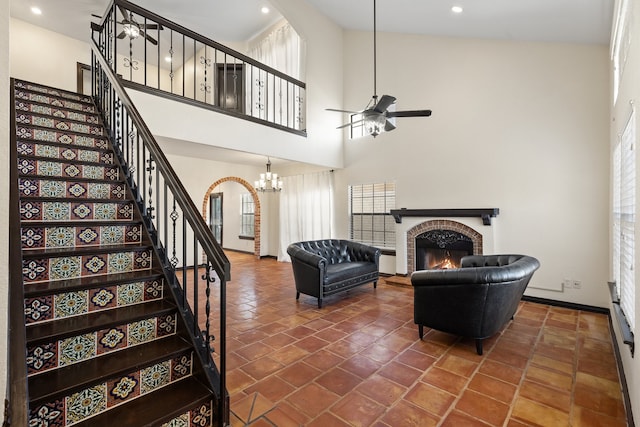 living room featuring high vaulted ceiling, ceiling fan with notable chandelier, plenty of natural light, and a brick fireplace