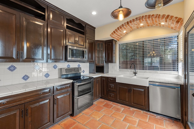 kitchen with tasteful backsplash, dark brown cabinets, appliances with stainless steel finishes, pendant lighting, and sink