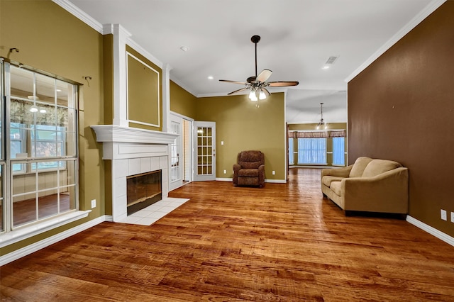 living room with ceiling fan, light wood-type flooring, crown molding, and a tiled fireplace