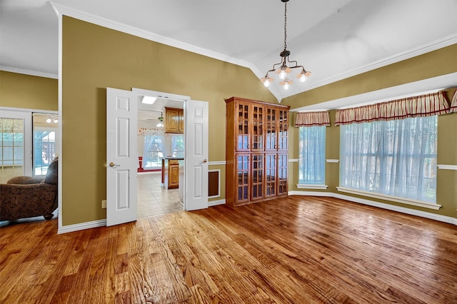 unfurnished dining area featuring wood-type flooring, ornamental molding, vaulted ceiling, and a wealth of natural light