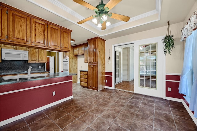 kitchen with dark tile patterned floors, ceiling fan, a tray ceiling, ornamental molding, and backsplash