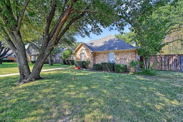 view of front of house with a front yard, brick siding, fence, and roof with shingles