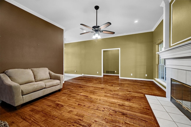 living room with ceiling fan, crown molding, light wood-type flooring, and a tiled fireplace