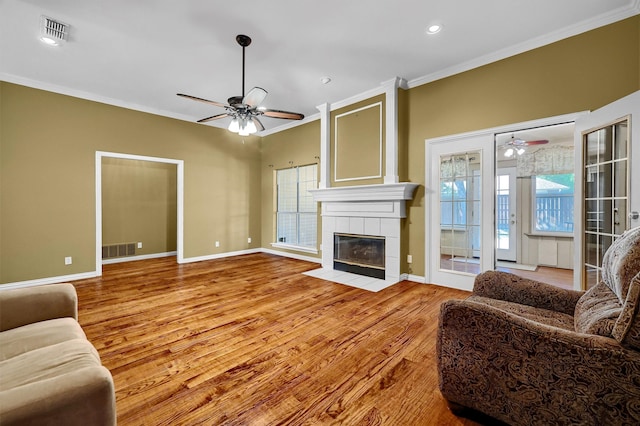 living room featuring ceiling fan, ornamental molding, light wood-type flooring, and a tile fireplace