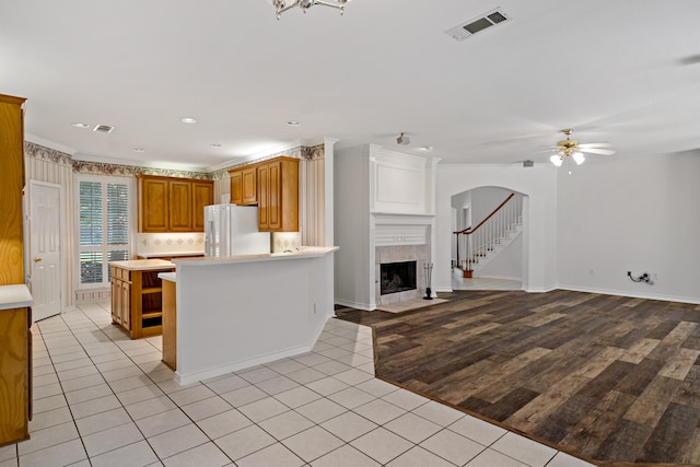 kitchen featuring light wood-type flooring, ceiling fan, a fireplace, crown molding, and white refrigerator