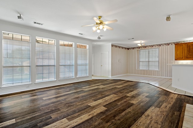 unfurnished living room with light wood-type flooring, crown molding, ceiling fan, and wood walls