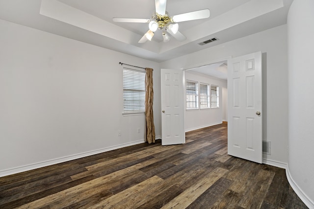 empty room featuring ceiling fan, a raised ceiling, and dark hardwood / wood-style flooring