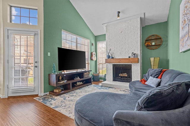 living room with high vaulted ceiling, a healthy amount of sunlight, a fireplace, and hardwood / wood-style floors