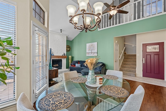 dining room with ceiling fan with notable chandelier, high vaulted ceiling, and wood-type flooring