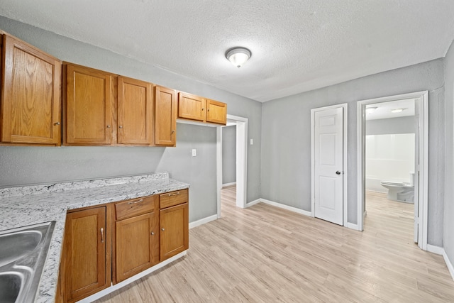 kitchen featuring sink, light stone countertops, a textured ceiling, and light wood-type flooring