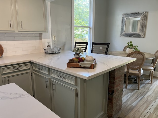 kitchen featuring light wood-type flooring, light stone countertops, gray cabinetry, kitchen peninsula, and backsplash