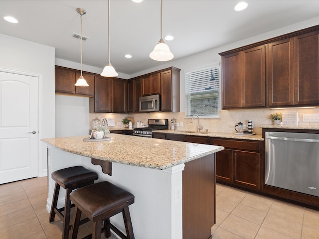 kitchen with a center island, stainless steel appliances, light stone counters, and hanging light fixtures