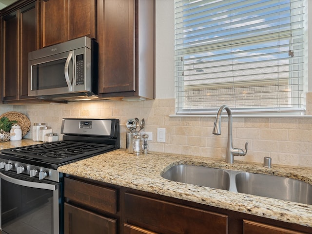 kitchen with light stone counters, sink, stainless steel appliances, and tasteful backsplash