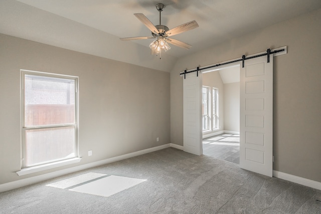 unfurnished room featuring lofted ceiling, ceiling fan, a barn door, and light carpet