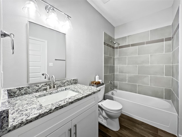 full bathroom with wood-type flooring, tiled shower / bath, vanity, and toilet