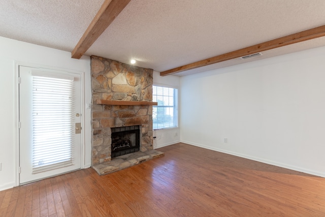 unfurnished living room with beamed ceiling, a textured ceiling, a fireplace, and hardwood / wood-style flooring