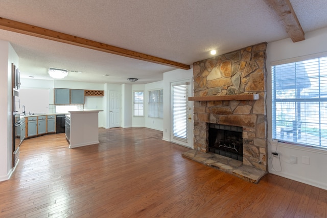 unfurnished living room with a stone fireplace, hardwood / wood-style flooring, a textured ceiling, and a wealth of natural light