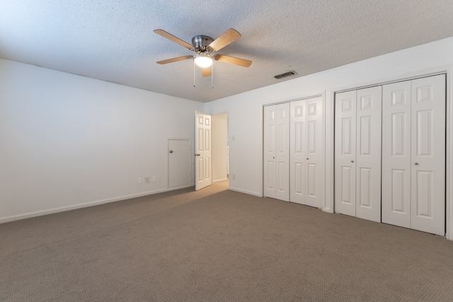 unfurnished bedroom featuring dark colored carpet, multiple closets, a textured ceiling, and ceiling fan