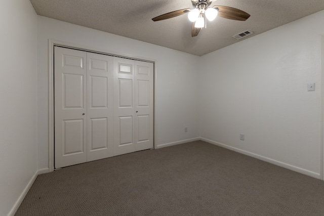 unfurnished bedroom with ceiling fan, a textured ceiling, a closet, and dark colored carpet