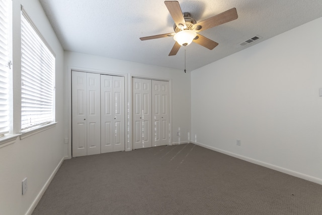 unfurnished bedroom with ceiling fan, two closets, dark carpet, and a textured ceiling