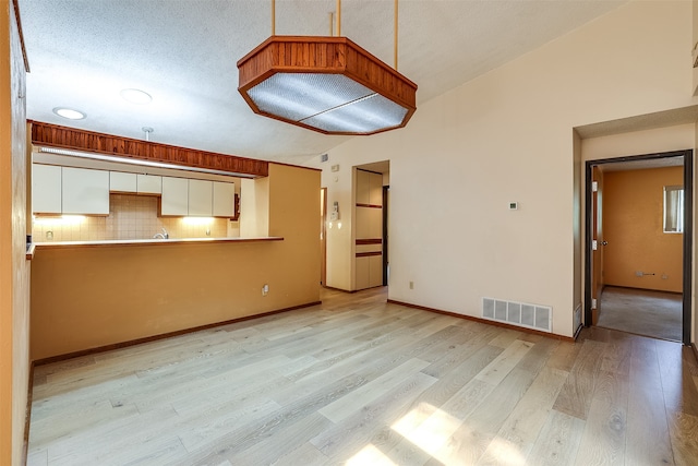 unfurnished living room featuring high vaulted ceiling, light wood-type flooring, and a textured ceiling