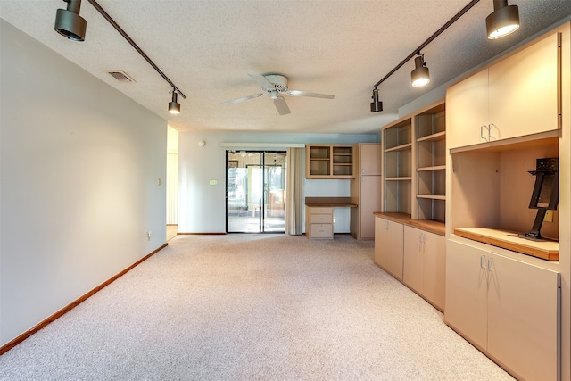 unfurnished living room featuring track lighting, ceiling fan, built in desk, and a textured ceiling