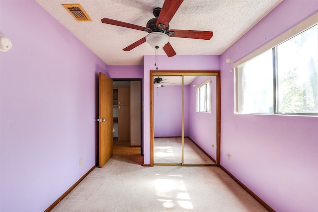 unfurnished bedroom featuring ceiling fan, light colored carpet, a textured ceiling, and a closet