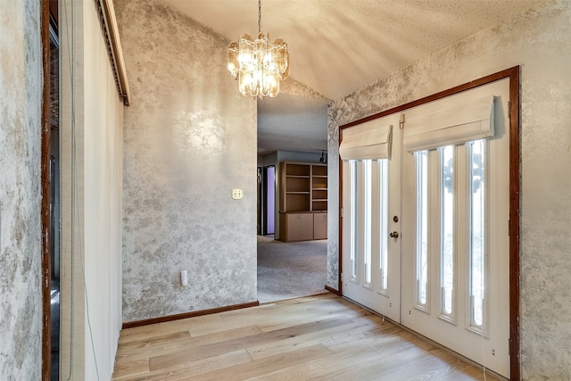 foyer entrance featuring a notable chandelier, vaulted ceiling, light hardwood / wood-style flooring, and a textured ceiling