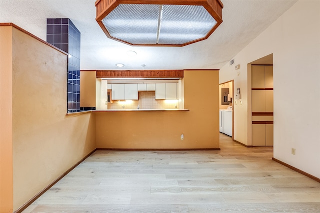 kitchen with kitchen peninsula, tasteful backsplash, a textured ceiling, white cabinetry, and light wood-type flooring